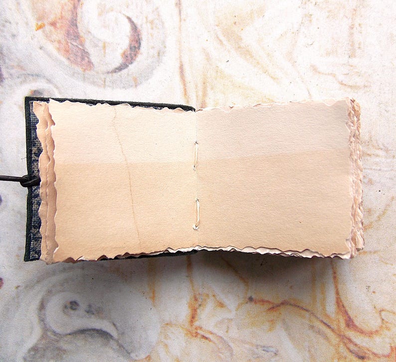 May include: A small, handmade book with a black fabric cover and blank, cream-colored pages. The pages have a rough, textured edge.