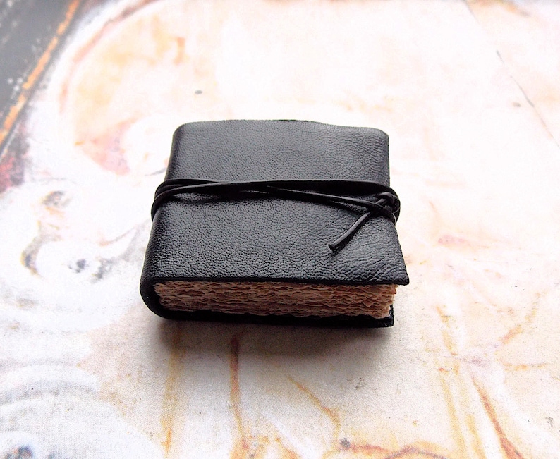 May include: A small black leather-bound journal with a brown paper interior and a black leather tie closure.