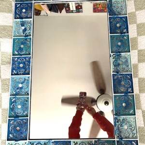May include: A rectangular mirror with a white frame and a blue and white tile border. The tiles have a floral design.
