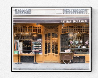May include: A storefront with a brown awning and gold trim. The sign above the door reads "Artisan Boulanger". The windows are decorated with pastries and flowers. A small cart with pastries is parked in front of the store.