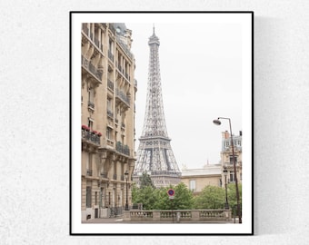 May include: A black and white photograph of the Eiffel Tower in Paris, France. The tower is seen from a street level perspective, with a building on the left side of the image and trees in the foreground.