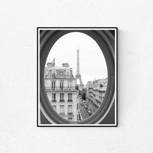 May include: Black and white photograph of the Eiffel Tower in Paris, France, seen through a round window.