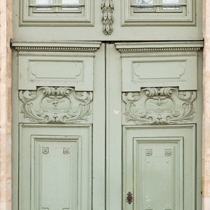 May include: A pair of antique, double doors with ornate carvings and a light green paint finish. The doors have a series of raised panels and are accented with decorative metal hardware.