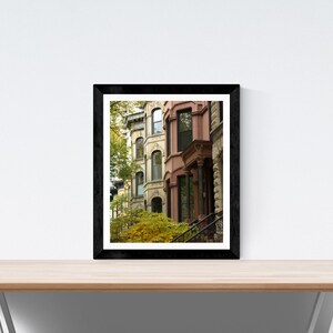 Puede incluir: Una fotograf&iacute;a enmarcada de una fila de edificios de ladrillo con puertas y ventanas de colores. Los edificios est&aacute;n en un entorno urbano y tienen un aspecto vintage. La foto est&aacute; en un marco negro.