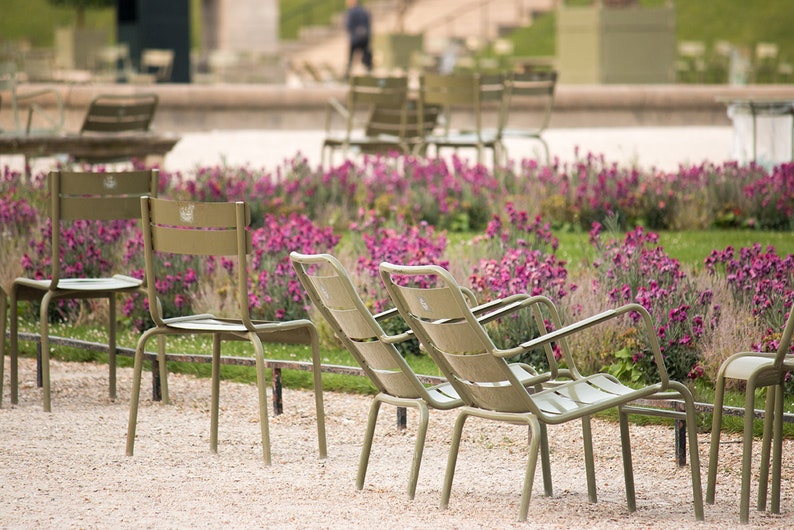 May include: A row of green metal chairs sit in a garden setting. The chairs are arranged in a semi-circle facing a bed of pink flowers.