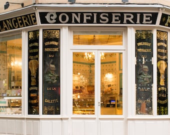 May include: A storefront with a white facade and gold lettering that reads "BOULANGERIE CONFISERIE PAT". The windows are decorated with gold and black lettering and images of wheat and a windmill.