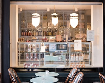 May include: A storefront with a sign that reads "Patissier - Salon de The" in gold lettering. The storefront has a large window display with shelves of pastries and other treats. There are tables and chairs set up outside the store.