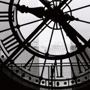 May include: Black and white photo of a large clock face with Roman numerals. The clock face is framed by a metal grid. The clock hands are in silhouette against a bright background.