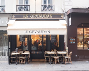 May include: A Parisian cafe called "Le Gévaudan" with a white awning and black framed windows. There are tables and chairs set up outside the cafe.