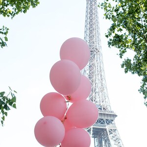 May include: A bunch of pink balloons tied together with a string, floating in front of the Eiffel Tower in Paris, France.