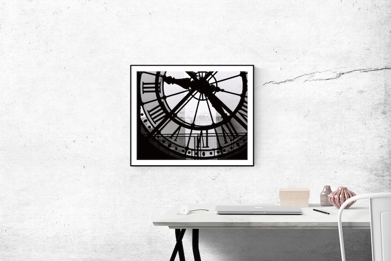 May include: Black and white photograph of a clock face with Roman numerals. The clock is framed in a black frame and is hanging on a white wall.