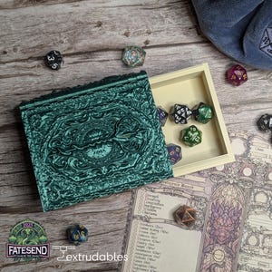 Peut inclure: Une boîte à dés ornée de couleur teal, avec un couvercle assorti, ouverte pour révéler divers dés à plusieurs faces. La boîte est posée sur une surface en bois avec une feuille de personnage et des dés supplémentaires éparpillés.