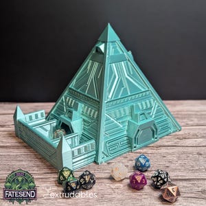 May include: A teal green pyramid-shaped dice tower with a detailed design. The tower has a small opening at the top and a larger opening at the bottom. The tower is sitting on a wooden surface with several dice scattered around it.