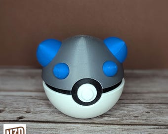 May include: A gray and white Poke Ball with blue ears. The Poke Ball has a black ring around the center.