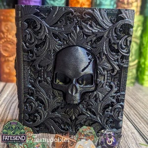 May include: A black, intricately carved box with a skull design. The box is made of a 3D printed material and has a glossy finish. The text "FATESEND YEAR OF THE SNAKE" is printed on the bottom of the box.