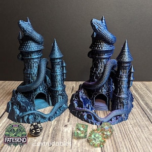 Puede incluir: Dos torres de dragón impresas en 3D de color azul y morado iridiscente con una serpiente enroscada alrededor. Las torres tienen una pequeña abertura en la base. Hay tres dados verdes delante de las torres.