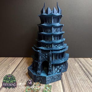 May include: A dark blue, multi-level pagoda-style dice tower with a detailed design. The tower is made of plastic and has a base with a hexagonal shape. The tower is sitting on a wooden surface with dice scattered around it.