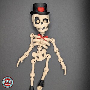 May include: A skeleton figurine wearing a black top hat with a red heart, a red bow tie, and a white skeleton body.