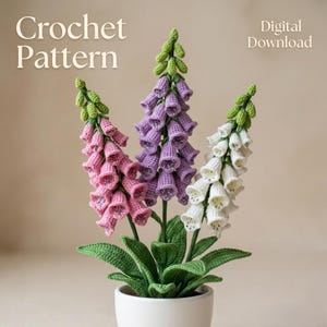 May include: A crochet pattern for a digital download. The image shows three crocheted foxglove flowers in a white pot. The flowers are pink, purple, and white with green leaves and stems. The text "Crochet Pattern" and "Digital Download" are visible.