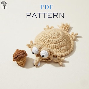 Pode incluir: Uma criatura bege de crochê com grandes olhos brancos e um focinho longo, ao lado de uma bolota marrom de crochê. O texto "PDF PATTERN" é exibido em azul na parte superior. Este é um padrão para um projeto de crochê.