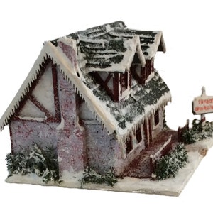 Peut inclure: Une miniature de chalet enneig&eacute; avec une chemin&eacute;e en brique rouge et une pancarte indiquant "L'atelier du P&egrave;re No&euml;l". Le chalet a un toit blanc avec des gla&ccedil;ons et une base enneig&eacute;e.