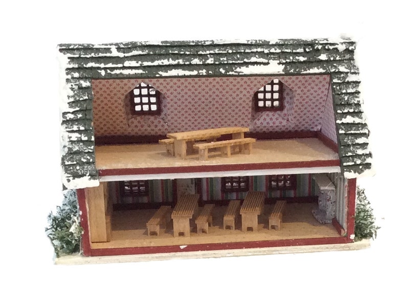Peut inclure: Une maison de poup&eacute;e miniature en bois avec un ext&eacute;rieur rouge et blanc et un toit vert. L'int&eacute;rieur est visible, montrant une pi&egrave;ce avec des meubles en bois et un papier peint &agrave; motifs.