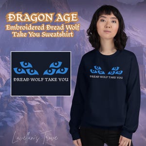 May include: Navy blue sweatshirt featuring the text "DRAGON AGE Embroidered Dread Wolf Take You Sweatshirt". The sweatshirt has a blue graphic of three sets of stylized eyes above the text "DREAD WOLF TAKE YOU".