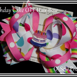 Puede incluir: Un lazo para el pelo rosa y blanco con un patr&oacute;n de lunares de colores y un dije de pastel de cumplea&ntilde;os que dice "Happy B.Day".