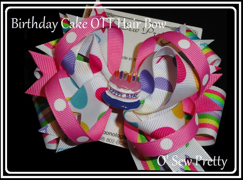 Puede incluir: Un lazo para el pelo rosa y blanco con un patr&oacute;n de lunares de colores y un dije de pastel de cumplea&ntilde;os que dice "Happy B.Day".