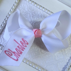 May include: White hair bow with a pink center and the name "Chanlee" embroidered in pink on the bow.