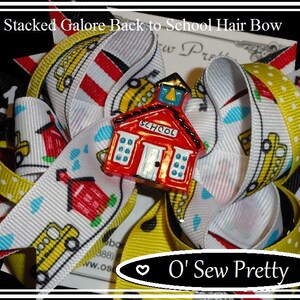 May include: Triple stacked hair bow with a red schoolhouse charm. The bow is made of white, yellow and red ribbon with a polka dot pattern. The ribbon has a school bus and schoolhouse print. The charm has the word "SCHOOL" on the front.