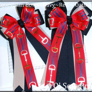 May include: Two red, white, and navy blue equestrian bows with gold snaffle bit accents. The bows are tied with a beige ribbon.