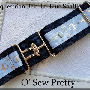 May include: A navy blue and light blue equestrian belt with a gold snaffle bit design and a gold buckle. The belt is made of ribbon and has a gold buckle. The text "O' Sew Pretty" is visible at the bottom of the image.