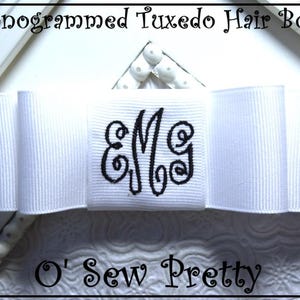 May include: A white monogrammed tuxedo hair bow with the letters "EMG" embroidered in black. The bow is made of a wide, ribbed ribbon. The text "Monogrammed Tuxedo Hair Bow" and "O' Sew Pretty" are visible.