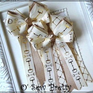 May include: Cream-colored ribbon bows with gold horse bit patterns. The bows have long, decorative tails and are arranged on a white background. The text "O' Sew Pretty" is visible at the bottom.