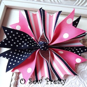 May include: A handmade hair bow featuring a layered design with pink, navy, and white ribbons. The bow has a mix of polka dots, stripes, and solid colors. The text "O Sew Pretty" is visible at the bottom.