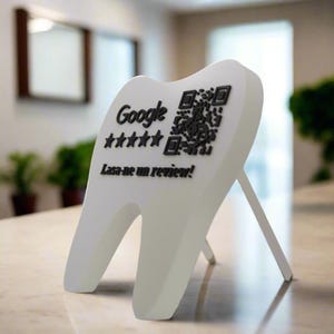 Può includere: Un cartello bianco a forma di dente con un codice QR e il logo Google, cinque stelle e la scritta "Lasa-ne un review!" in nero. Il cartello è sostenuto da un supporto bianco.
