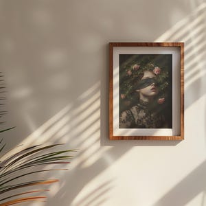 May include: A framed art print depicting a person with a blindfold and a floral crown. The portrait is set against a dark backdrop, with the person wearing a black lace top. The frame is made of wood.