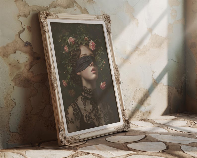 May include: A framed portrait of a woman wearing a black blindfold, with a floral crown of pink roses and green leaves. The artwork is in an ornate, cream-coloured frame, leaning against a textured wall.