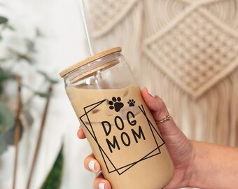 May include: A clear glass tumbler with a bamboo lid and a straw. The tumbler has a black and white graphic that says "Dog Mom" with paw prints.