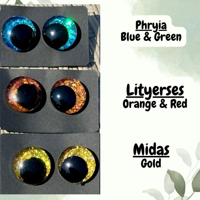 Op de afbeelding: Drie paar ronde cabochon-ogen op zwarte displaykaarten. Het bovenste paar is Phryia Blue & Green, het middelste paar is Lityerses Orange & Red en het onderste paar is Midas Gold. Elk oog heeft een grote zwarte pupil en een glinsterende iris.