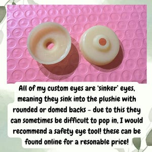 Op de afbeelding: Twee ronde, gebroken witte, semi-transparante plastic sinker-ogen voor knuffels. E&eacute;n oog wordt getoond vanaf de holle onderkant met een centraal gat, en het andere vanaf de bolle, gewelfde bovenkant met een centraal gat voor bevestiging.