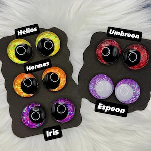 Op de afbeelding: Zes paar ronde hars cabochons met glitterende, veelkleurige irissen en grote zwarte pupillen. De sets zijn gelabeld als Helios, Hermes, Iris, Umbreon en Espeon, weergegeven op twee zwarte kaarten met een glanzende, reflecterende afwerking.