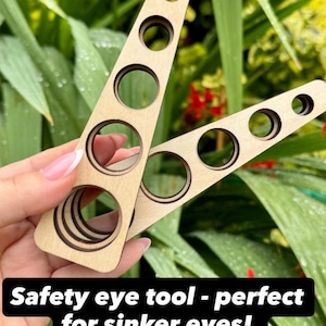 Op de afbeelding: Een veiligheidsoog-gereedschap van lichtgekleurd hout, bestaande uit twee driehoekige delen met vijf ronde uitsparingen van verschillende diameters. De tekst op de afbeelding luidt: Safety eye tool - perfect for sinker eyes! 5 different sizes to suit most eye backings!