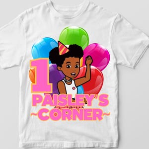 May include: White t-shirt with a pink number one, a cartoon girl with a party hat and balloons, and the text "Paisley's Corner".