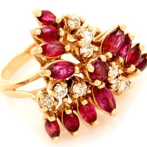 Puede incluir: Un anillo de oro con un grupo de rubíes talla marquesa y diamantes redondos. Los rubíes son de color rojo intenso y los diamantes brillan. El anillo tiene un diseño floral único.