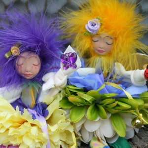 May include: Two handmade dolls with purple and yellow hair, wearing white dresses and holding flowers. The doll with purple hair is holding a butterfly charm, and the doll with yellow hair is holding a ladybug charm.