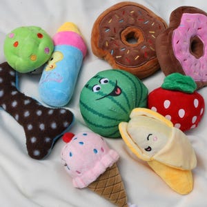 May include: A collection of plush dog toys in various shapes and colors. Includes a bone, a green ball, a blue bottle, a watermelon, a strawberry, a banana, two donuts, and an ice cream cone.