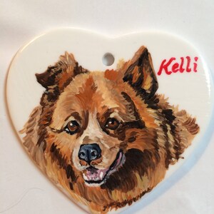 May include: A hand-painted heart-shaped ceramic ornament featuring a portrait of a brown and white dog with the name "Kelli" written in red.