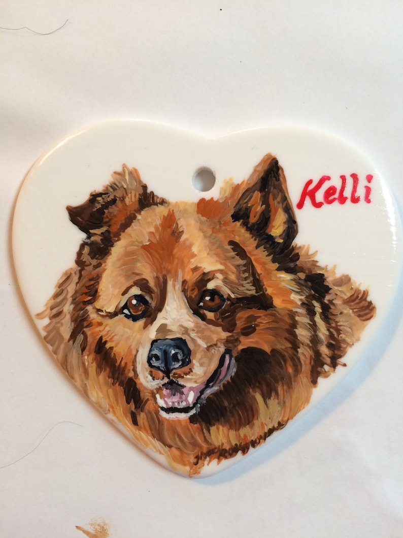 May include: A hand-painted heart-shaped ceramic ornament featuring a portrait of a brown and white dog with the name "Kelli" written in red.